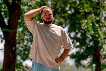 Portrait of a young guy tired of rollerblading against the background of trees in the park plus...