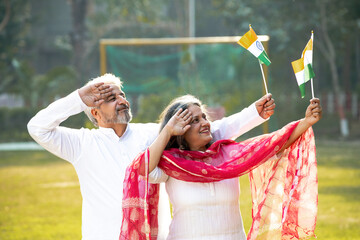 Indian senior couple saluting of tricolor flag together at garden.