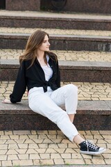 Portrait of a young and attractive happy girl sitting on the steps on a summer day in casual clothes.