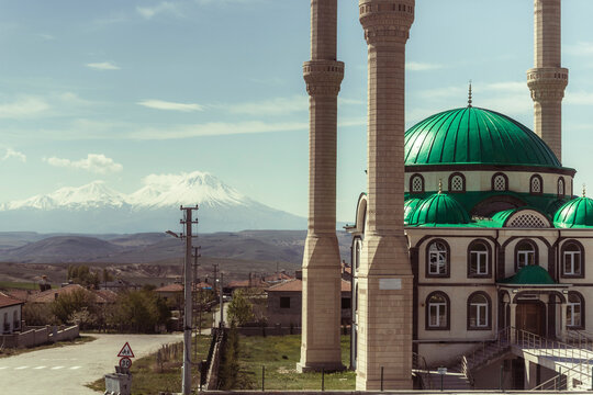 View of Mount Hasandagi, a Mountain Peak and inactive volcano with snow on the top with a green dome mosque in foreground, Aksaray, Turkey.