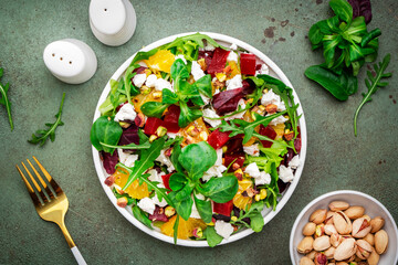 Beet and feta cheese salad with arugula, lettuce, orange and pistachios on green table. Fresh...