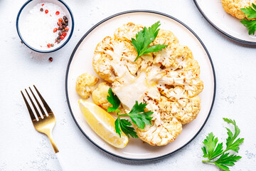 Vegan steak from baked cauliflower with garlic butter, parley and spice on plate, white table background, top view