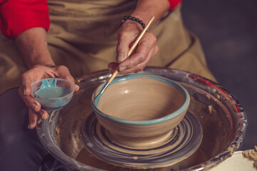Closeup of woman painting clay mug, coloring pottery in workshop with a paintbrush.