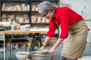 Woman potter taking finished plate from pottery wheel, making earthenware.