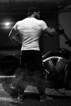 Athletic bearded biker man posing with motorbike with his back to the frame