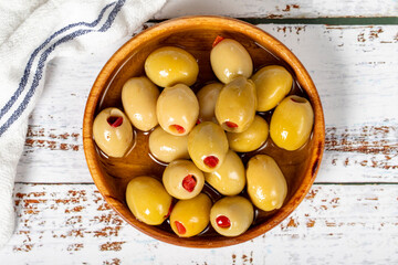 Pepper-stuffed green olives at wooden bowl. Olives on a white wood background. Mediterranean food. vegan food. Top view - Powered by Adobe