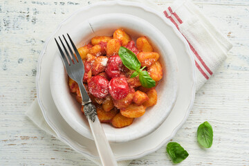 Potato gnocchi. Traditional homemade potato gnocchi with tomato sauce, basil and parmesan cheese on kitchen table on light grey kitchen table background. Traditional Italian food. Top view.