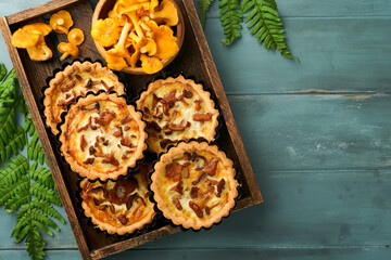 Savory hands pie with chanterelle mushrooms, cream and cheese on cutting board on rustic old wooden table background. Homemade tarts with seasonal chanterelle mushrooms. Rustic style. Top view.