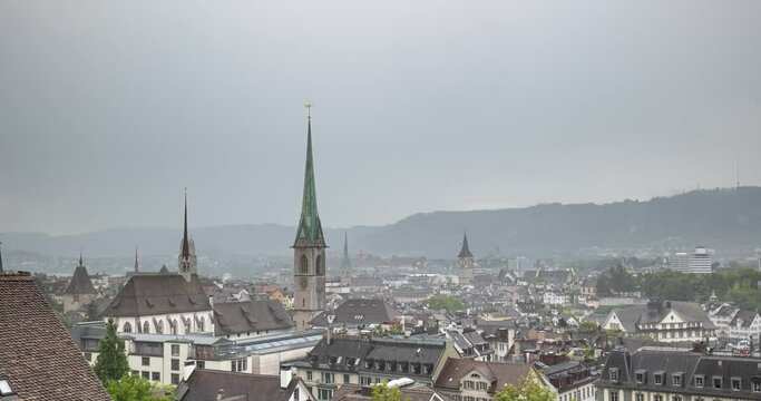 Left to right dynamic panning  time lapse of Zurich city Switzerland. Rainy summer day, aerial viewpoint, rooftops, church towers, hills in the background