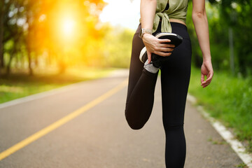A young sporty woman stretching her legs and exercising before running to protect pain and injury in the park.