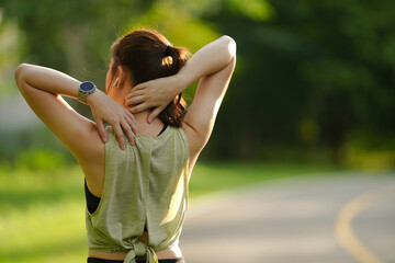 A young female athlete in sport top kneads and massages her neck with her hands while jogging in the park. Woman with back pain neck injurytrauma during workout.