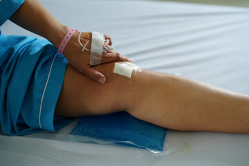 Close up knee replacement surgery after operation patient with saline drip in a hand on the bed in hospital.