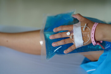 Close up left hand of patient with Saline intravenous using ice gel pack put on right knee on the...