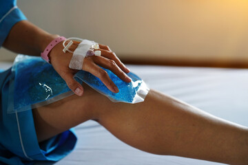 The patient's hand in the hospital with a brine line piercing sitting on the bed holding blue gel ice pack on the knee.