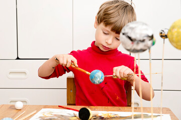 Boy painting styrofoam balls when making model of Solar System for school. Science project at home. Concept of teaching children. Developing creativity from an early age. Drawing with brushes and pain