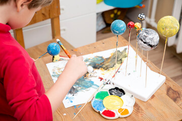 Boy painting styrofoam balls when making model of Solar System for school. Science project at home. Concept of teaching children. Developing creativity from an early age. Drawing with brushes and pain - obrazy, fototapety, plakaty