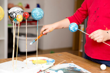 Boy painting styrofoam balls when making model of Solar System for school. Science project at home. Concept of teaching children. Developing creativity from an early age. Drawing with brushes and pain