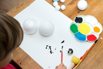 Boy painting styrofoam balls when making model of Solar System for school. Science project at home....