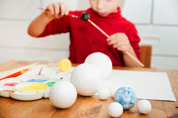 Boy painting styrofoam balls when making model of Solar System for school. Science project at home....