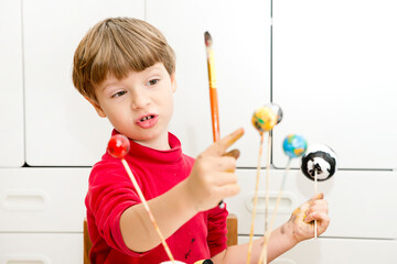 Boy painting styrofoam balls when making model of Solar System for school. Science project at home....