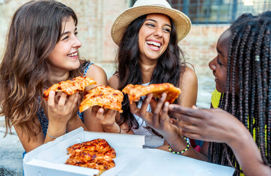 Three Young Female Friends Eating Pizza Sitting Outside - Happy Women Enjoying Street Food In The City - Italian Food Culture And European Holidays Concept