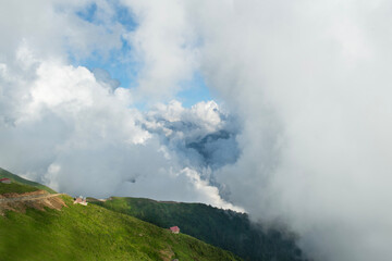 Cloudy mountains.
Mountains in clouds at sunrise in summer. Aerial view of mountain peak with green trees in fog. Top view of mountain valley in low clouds from drone. Rize Huser plateau, Türkiye