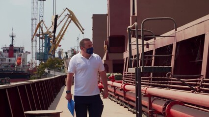 Shipping agent walks down the bulker ship and inspects loading at sea port. Expeditor goes on cargo vessel in face mask. Global trading and shipment concept.