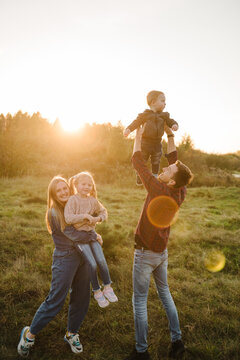Mother, father, daughter, son walks in grass in spring field at sunset. Childs embrace parents. Family spending time together in nature. Parents hold in hands, throw up happy kids into sky autumn day.