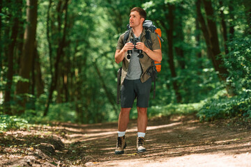 Standing and holding binoculars. Tourist in summer forest. Conception of exploration and leisure