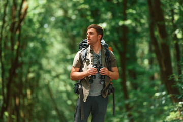 Standing and holding binoculars. Tourist in summer forest. Conception of exploration and leisure