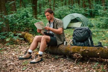 Sitting and looking at map. Tourist in summer forest. Conception of exploration and leisure