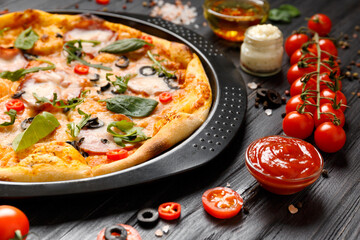 Pizza on a black dish on a dark wooden background.