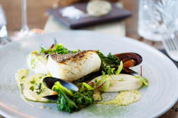 Cod fillet with cauliflower cream, asparagus, clam-wine sauce and mussles. Delicious seafood fish closeup served on a table for lunch in modern cuisine gourmet restaurant
