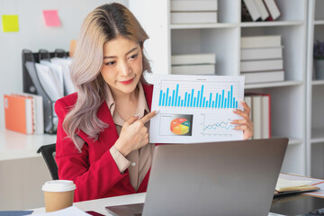 Asian businesswoman presenting a profitable company marketing plan with confidence at the office and future investment plans of the company with charts and graphs on the board.