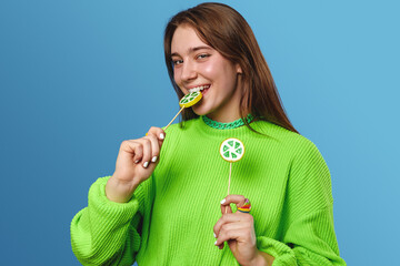 Cheerful young lady with brown hair, wearing green sweater smiling happily and making funny face...
