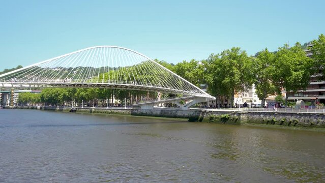 Bilbao, SPAIN - July 19 2022: Zubizuri Bridge, also called the Campo Volantin Bridge. is a tied arch footbridge across the Nervion River in Bilbao, Spain. People passing. Stabilized static video