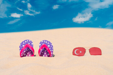 Sunglasses with glasses in the form of the flag of Turkey and flip-flops lie on the sand against...