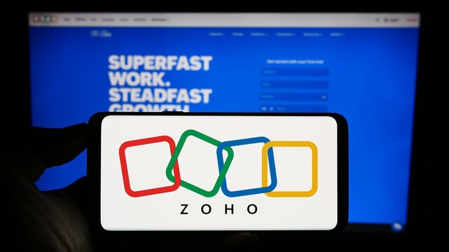 Stuttgart, Germany - 07-28-2023: Person holding cellphone with logo of Indian technology company Zoho Corporation on screen in front of business web page. Focus on phone display.