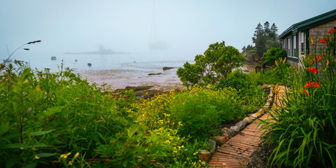 Foggy seascape with moored yacht and boat, vibrant garden plants and flowers at a coastal village in Maine