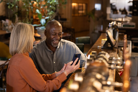 Senior couple on a date in a wine bar looking at a smartphone together laughing