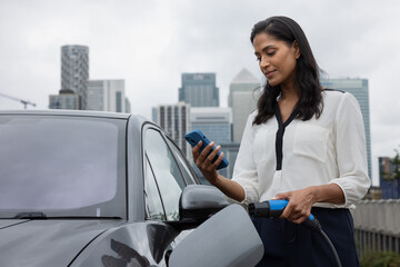 Businesswoman charging electric car in city with view of London skyline