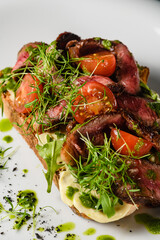 Bruschetta with meat, tomatoes, herbs, cheese, pesto sauce on a white plate.