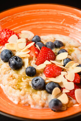 Oatmeal with blueberries, almonds and strawberries in an orange plate.