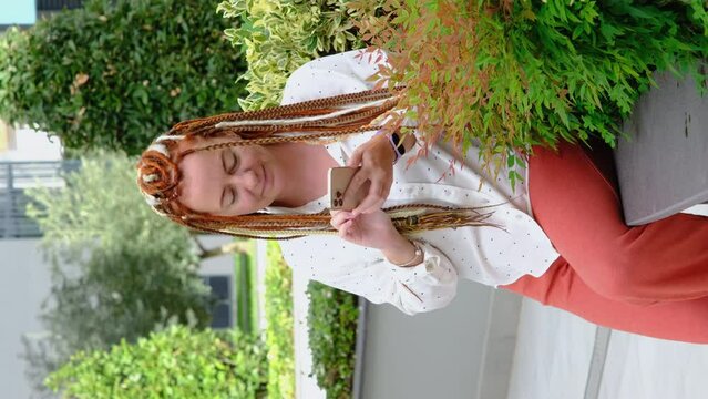 Modern young woman with headlock using mobile phone, texting on smart phone sitting in city park. 