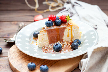Slice of vanilla cheesecake with salted caramel sauce, fresh raspberry, blueberry and nuts on grey star plate, close up view