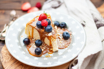 Slice of vanilla cheesecake with salted caramel sauce, fresh raspberry, blueberry and nuts on grey star plate, close up view