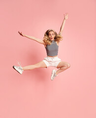 Full body photoshoot of happy young woman looking at camera and jumping against light pink studio background.