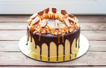 Peanut butter cream cake with melted chocolate, candy bars, bites of peanuts and salted caramel on wooden background