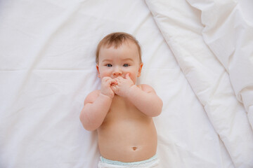 a cute cheerful newborn baby in a diaper is lying on his back on a white sheet. view from above. lifestyle. High quality photo