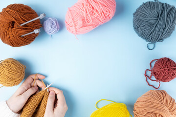 Woman in white sweater knits yellow yarn scarf, various ball of yarn on table. Top view. Copy space